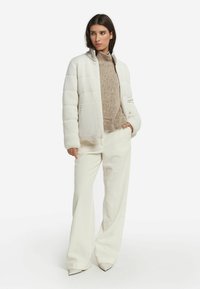 Witte gewatteerde donsjas met zijzakken, gecombineerd met een beige gebreide trui en ivoorkleurige ribgebreide wide-leg broek, met pumps met een spitse neus.