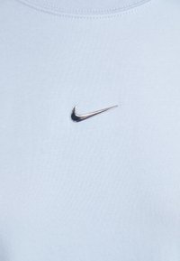 T-shirt Nike azul claro com uma textura suave e corte clássico; apresenta um logótipo swoosh metálico no peito.