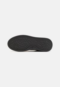 Semelle de chaussure noire avec motif de bande de roulement en forme de losange sur un fond blanc plat, vue du dessous.