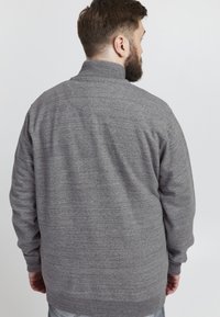 Maglione in fleece grigio con colletto alto, caratterizzato da un tessuto testurizzato e polsini a coste. La vista posteriore mostra una vestibilità comoda e dettagli delle cuciture.