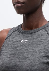 Κοντινό πλάνο ενός ατόμου που φοράει γκρι αμάνικο αθλητικό τοπ με μικρό λευκό λογότυπο Reebok στο στήθος.