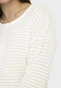 Witte top met lange mouwen en gouden horizontale strepen, met een relaxed fit en een zachte textuur. De halslijn is breed en rond.