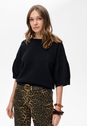 Czarny,oversized sweter wykonany z dzianiny z szerokimi rękawami, zestawiony z legginsami w panterkę. Podkreślony brązowym paskiem i wieloma bransoletkami.