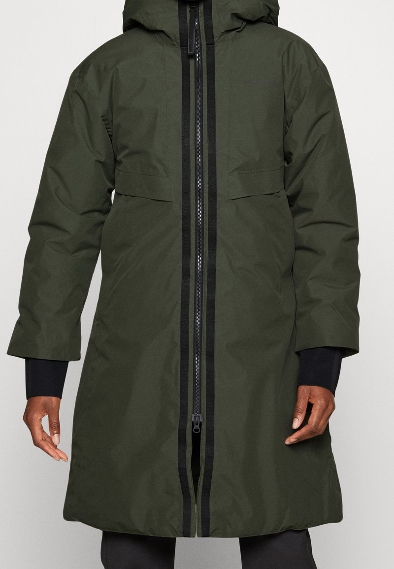 Manteau à capuche vert foncé avec manches longues, fermeture éclair noire sur le devant, et poignets intérieurs noirs porté par une personne à la peau foncée.