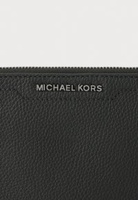 Must mustra rahakott tekstureeritud viimistlusega, millel on tõmblukk ja esiküljel hõbedane reljeefne "MICHAEL KORS" logo.