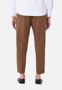 Pantaloni marroni a gamba affusolata con risvolti, abbinati a sneakers nere. Tessuto liscio, con pieghe frontali e una vestibilità casual.