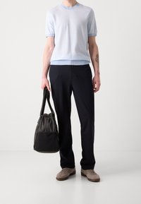 Suéter de punto de manga corta en azul claro, pantalones negros a medida, zapatillas gris y un bolso de hombro gris oscuro. Textura suave en toda la prenda.