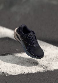 Zapatilla de running Nike con parte superior de un púrpura oscuro que presenta un patrón moteado, diseño ligero y una suela gris clara con acentos azules.