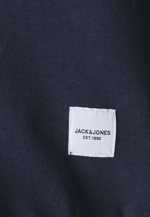 Granatowa tkanina z teksturowanym splotem; na materiale jest wszyta biała metka z napisem "JACK & JONES EST. 1990".