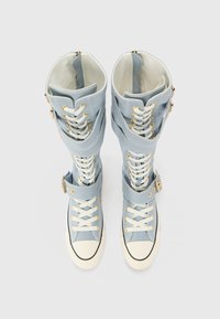 Blå kanvas høytopp sneakers med hvite gummisåler, hardware i gulltone og flere stropper. Teksturert materiale og særegen snøringsdesign.