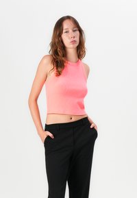 Pink cropped tank top with a ribbed texture, paired with black tailored trousers featuring side pockets and a smooth finish.