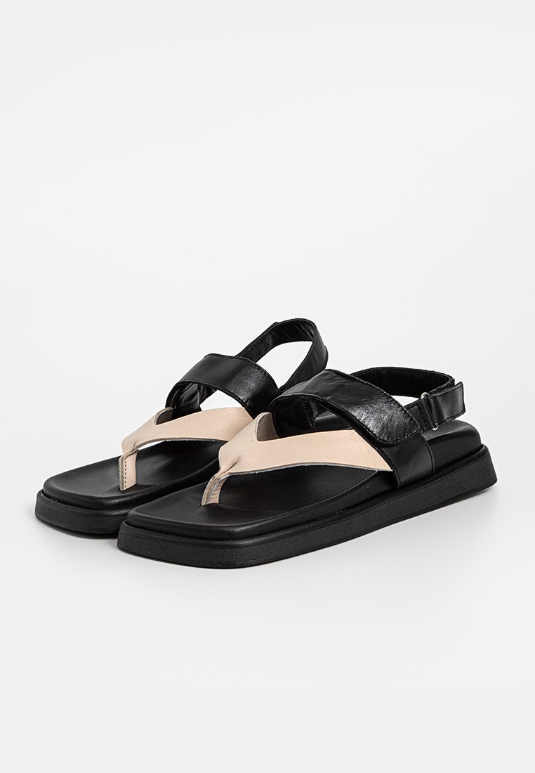 Schwarz-beige flache Sandalen mit breiten Riemen, Zehenring und verstellbarem Fersenriemen, auf einem weißen Hintergrund präsentiert.