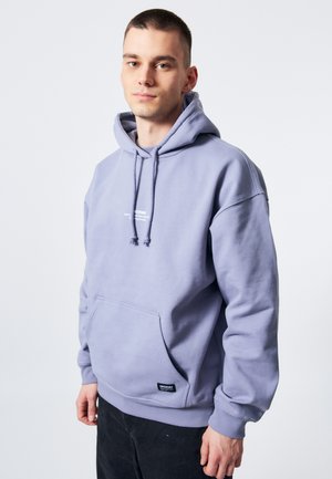 Lys lilla hættebluse med forlommeslomme, snore og logo. Stoffet ser blødt og struktureret ud, med ribbede manchetter og kant.