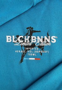 Turkooise stof met witte en zwarte tekst en silhouetten. Details omvatten "LIMITED EDITION," "IMPORT," en alcoholgehalte met kleuraccenten.