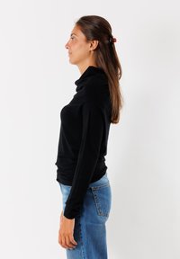 Maglione nero a maniche lunghe e collo alto con una vestibilità comoda, texture morbida e una leggera drappeggiatura sul colletto, abbinato a jeans blu.