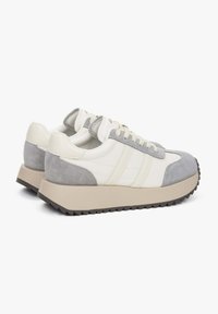 Sportieve sneakers met een lichtgrijs suède en witte leren bovenkant, voorzien van subtiele stiksels, crèmekleurige veters en een dikke beige rubberen zool.