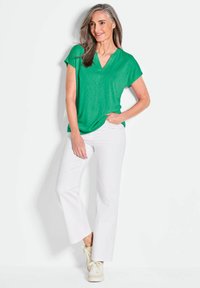 Groen T-shirt met korte mouwen en een V-hals, gecombineerd met witte rechte broek en lichte sneakers. Gladde, lichtgewicht stof met een relaxte pasvorm.