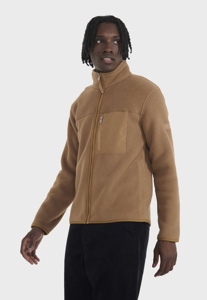 Braune Fleecejacke mit hohem Kragen, Reißverschluss vorne und strukturiertem Stoff. Verfügt über eine sandfarbene Brusttasche und kontrastierende gelbe Nähte.