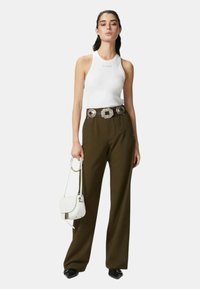 Top bianco senza maniche con logo, pantaloni a vita alta verde oliva con gamba ampia, cintura argentata con fibbia quadrata e una piccola borsa bianca.