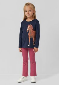 Langarm-Navy-Shirt mit einem Pferde-Graphic, kombiniert mit rosa gerippten Hosen und weißen Sneakern mit ausgeprägten Schnürsenkeln.