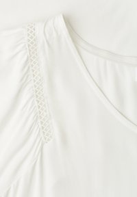 Tissu blanc avec encolure en V et bordure en dentelle verticale le long de la couture froncée de la manche.