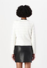 Pull en maille texturée blanc avec des manches longues, associé à une mini jupe en cuir noir. Des lignes épurées et des détails subtils sont visibles.