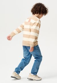 Gestreiftes beiges und weißes Langarmshirt, blaue Jeans und beiges Sneakers mit Mesh. Grafisches Detail auf dem Rücken des Shirts.