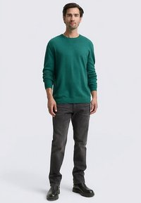 Zielony sweter z miękkiego materiału, w połączeniu z ciemnoszarymi jeansami. Sweter ma okrągły dekolt i długie rękawy. Całość dopełniają czarne buty.