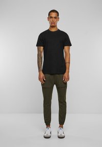 Zwarte T-shirt met een klassieke pasvorm en korte mouwen, gecombineerd met olijfgroene cargojoggers met zijzakken en elastische manchetten. Witte sneakers.