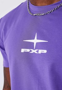 Camiseta de algodón morada con un logo gráfico blanco "PXP" y un diseño de estrella en la parte frontal. Textura suave con mangas cortas.