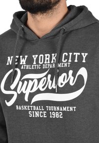Grijze hoodie met een voorkantgrafiek met "New York City Athletic Department" en "Superior Basketball Tournament Since 1982" in het wit.