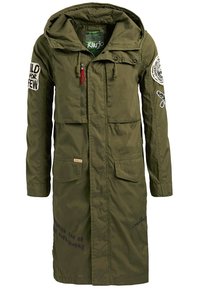 Olivgrön parkajacka med huva, utrustad med broderade lappar, dragkedja och fickor med klaff, samt textdetaljer på framsidan och ärmarna.