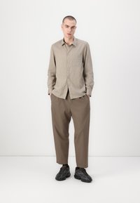Lys beige skjorte med vertikale striper, kombinert med løstsittende brune bukser og svarte teksturerte joggesko.