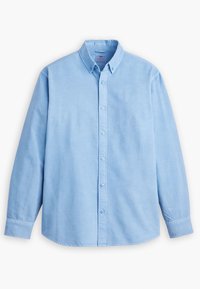 Chemise bleu clair en tissu de coton avec des manches longues, un col à boutons et un logo discret brodé sur la poitrine.