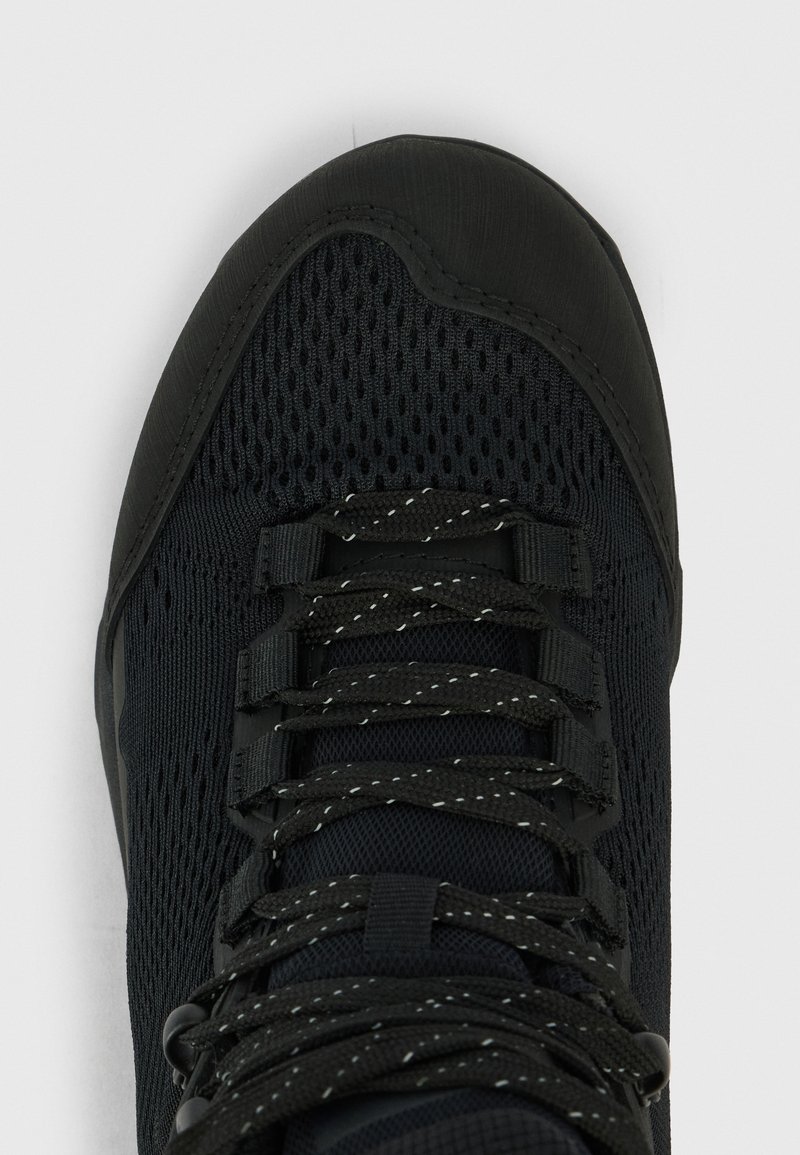 Czarne siatkowe buty sportowe z odblaskowymi sznurówkami związanymi, z wzmocnionym czubkiem i tkaninowymi pętlami do wiązania.