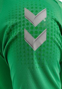 Grön sporttröja med en texturerad tyg med prickmönster. Två grå chevron-designs är tydligt synliga på baksidan.