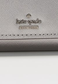 Szary skórzany portfel o teksturowanym wykończeniu, z metalową płytką z logiem "kate spade NEW YORK" i widocznymi d stitching.