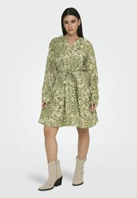 Groene jurk met een patroon, een strakke taille, lange mouwen en een V-hals, gecombineerd met beige cowboylaarzen en een gladde textuur.