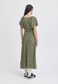 Blommig maxiklänning med korta volangärmar i grön och svart, med en figurnära midja och en fladdrande kjol, i kombination med svarta sneakers och krämfärgade strumpor.