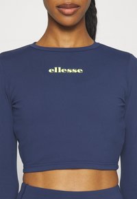 Top cropped de manga larga en color navy con un escote redondo y un logo en color amarillo claro en el pecho. Confeccionado en una tela suave y elástica.