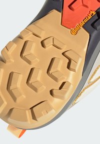 Σόλα παπουτσιού από μπεζ καουτσούκ με πολυκατευθυντικές προεξοχές, με μαύρη άκρη και πορτοκαλί λεπτομέρεια, που φέρει την επωνυμία "Continental" σε κίτρινο χρώμα.
