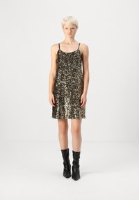 Vestido dourado de lantejoulas com alças pretas ajustáveis, bainha ampla e textura suave, combinado com botas pretas até ao joelho.