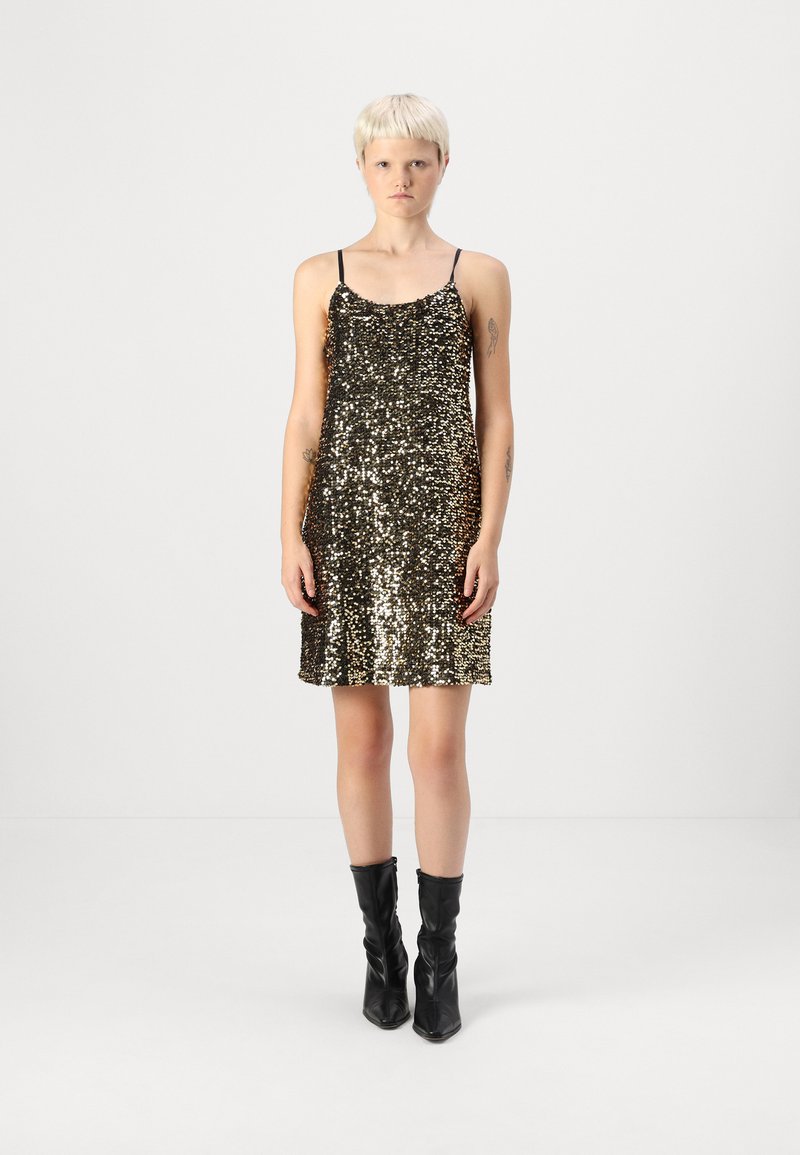 Vestido dourado de lantejoulas com alças pretas ajustáveis, bainha ampla e textura suave, combinado com botas pretas até ao joelho.