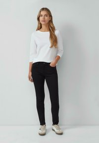 Zwarte jeans gecombineerd met een wit overhemd met lange mouwen en beige sneakers. De jeans hebben een slim fit en standaard zakken.