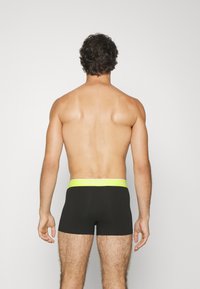 Fekete boxeralsó neon sárga Lacoste logós derékkal, minimalista dizájn, pamut keverék anyag, és szoros illeszkedés.