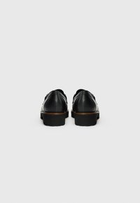 Zapatos de cuero negro con una textura suave, forma redondeada y suelas de goma resistentes. Presentan costuras sutiles y un tacón modesto.