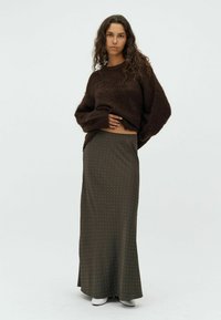 Smeđa vunena veste u kombinaciji s dugom maslinasto zelenom suknjom koja ima bijele točkice. Model nosi bijele čizme do gležnja. Jednostavan, minimalistički dizajn.