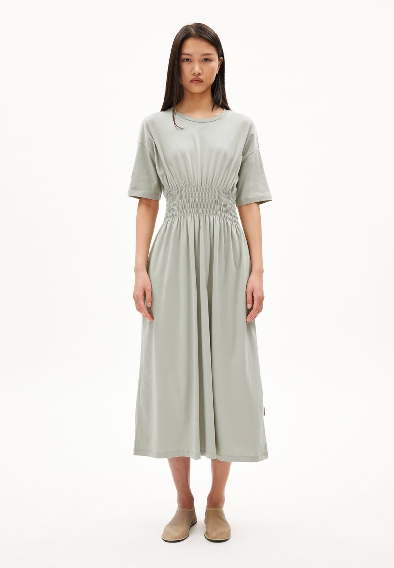 Light green cotton dress featuring a relaxed fit, short sleeves, and a smocked waist, extending to a midi length with a smooth texture.