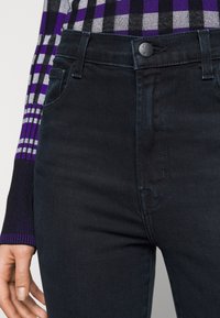 Jean en denim noir avec une taille ajustée, doté d'une fermeture à bouton en métal et de poches traditionnelles. Texture lisse avec un minimum de coutures visibles.