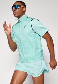 Lightweight mint green athletic jacket with a zip closure and short sleeves, paired with matching shorts. Sunglasses have blue tinted lenses.
